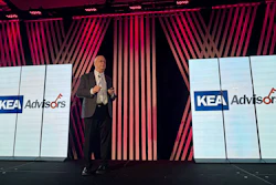 Professional speaker presenting at corporate event with KEA Advisors branding displayed on large screens