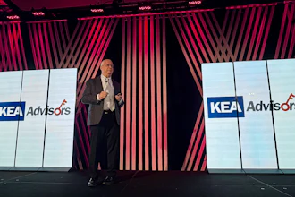 Professional speaker presenting at corporate event with KEA Advisors branding displayed on large screens