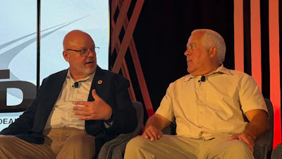 Two men in business attire participate in a panel discussion on stage with modern backdrop design.