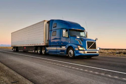 Blue Volvo semi-truck with refrigerated trailer driving on desert highway at sunset