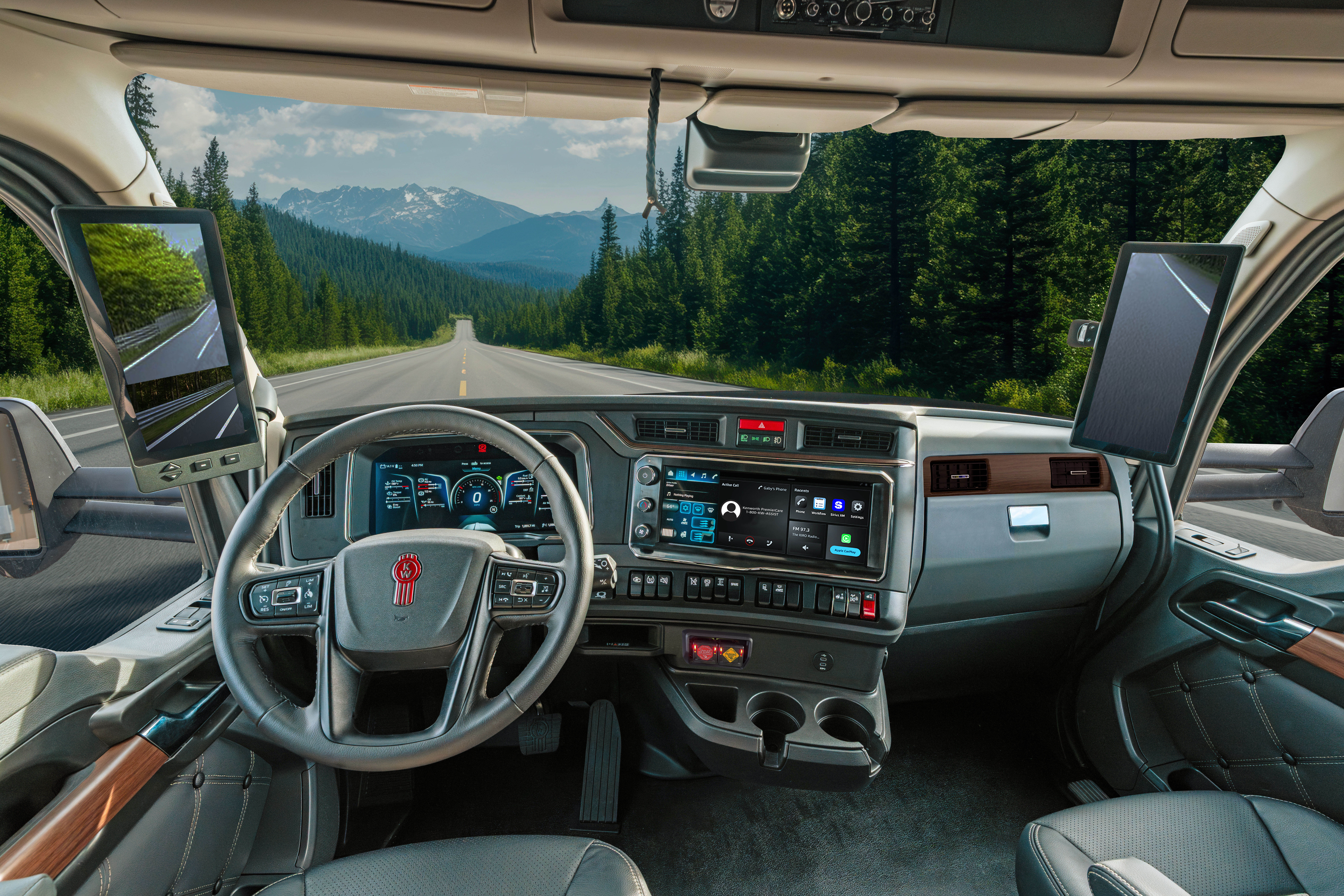 Interior view of commercial truck cabin with steering wheel, dashboard, and mountain landscape visible through windshield
