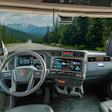 Interior view of commercial truck cabin with steering wheel, dashboard, and mountain landscape visible through windshield