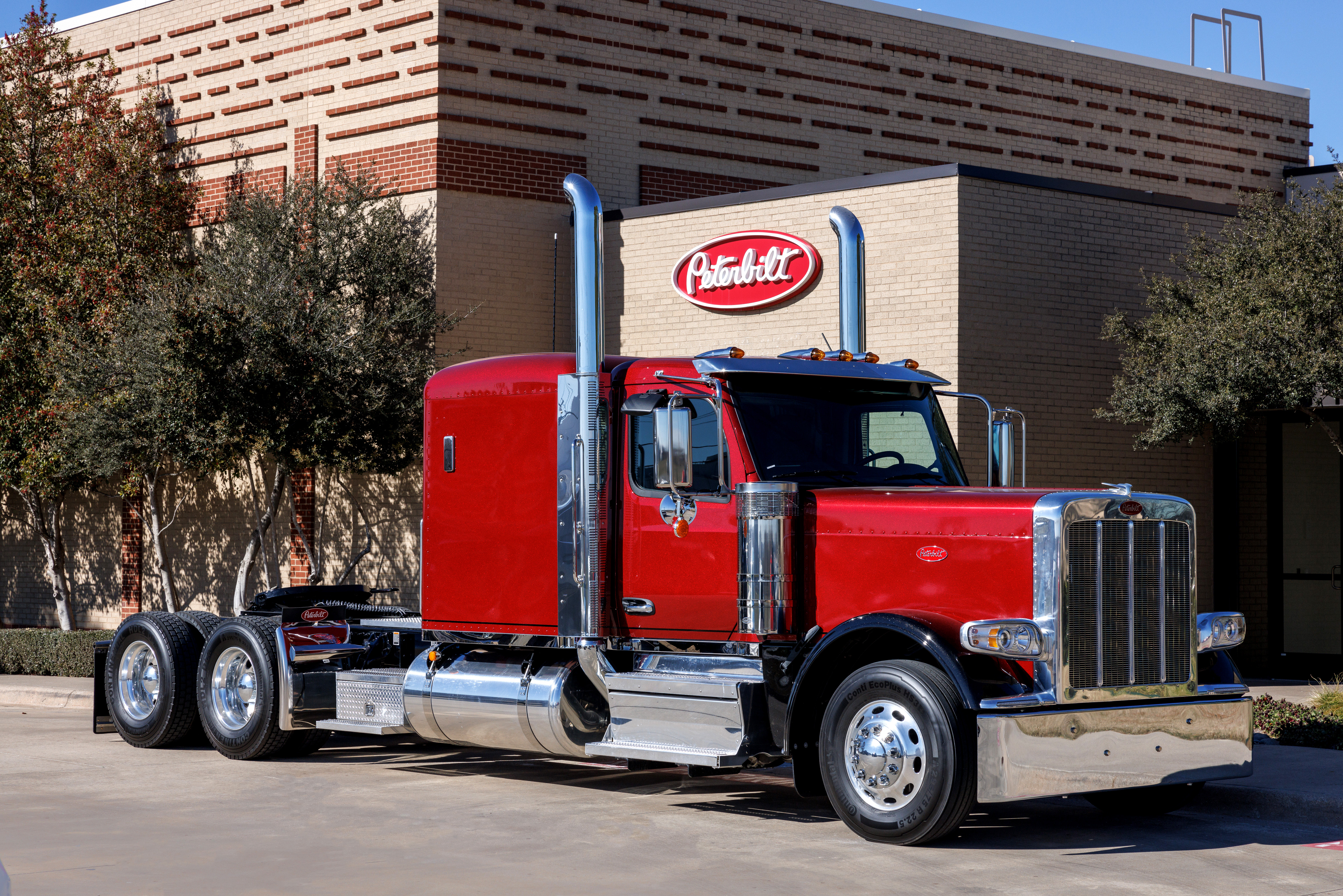Red and black Peterbilt semi-truck parked in front of a brick building with Peterbilt signage