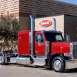 Red and black Peterbilt semi-truck parked in front of a brick building with Peterbilt signage