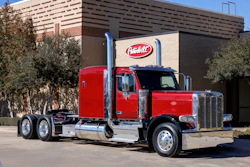 Red and black Peterbilt semi-truck parked in front of a brick building with Peterbilt signage