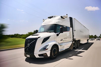 White Volvo semi-truck driving on highway with green landscape and blue sky