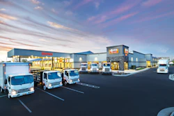 Isuzu commercial vehicle dealership facility at dusk with three white delivery trucks parked in front of modern building