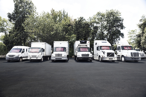 Fleet of white commercial delivery vans and trucks lined up in a row with trees in background