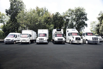 Fleet of white commercial delivery vans and trucks lined up in a row with trees in background