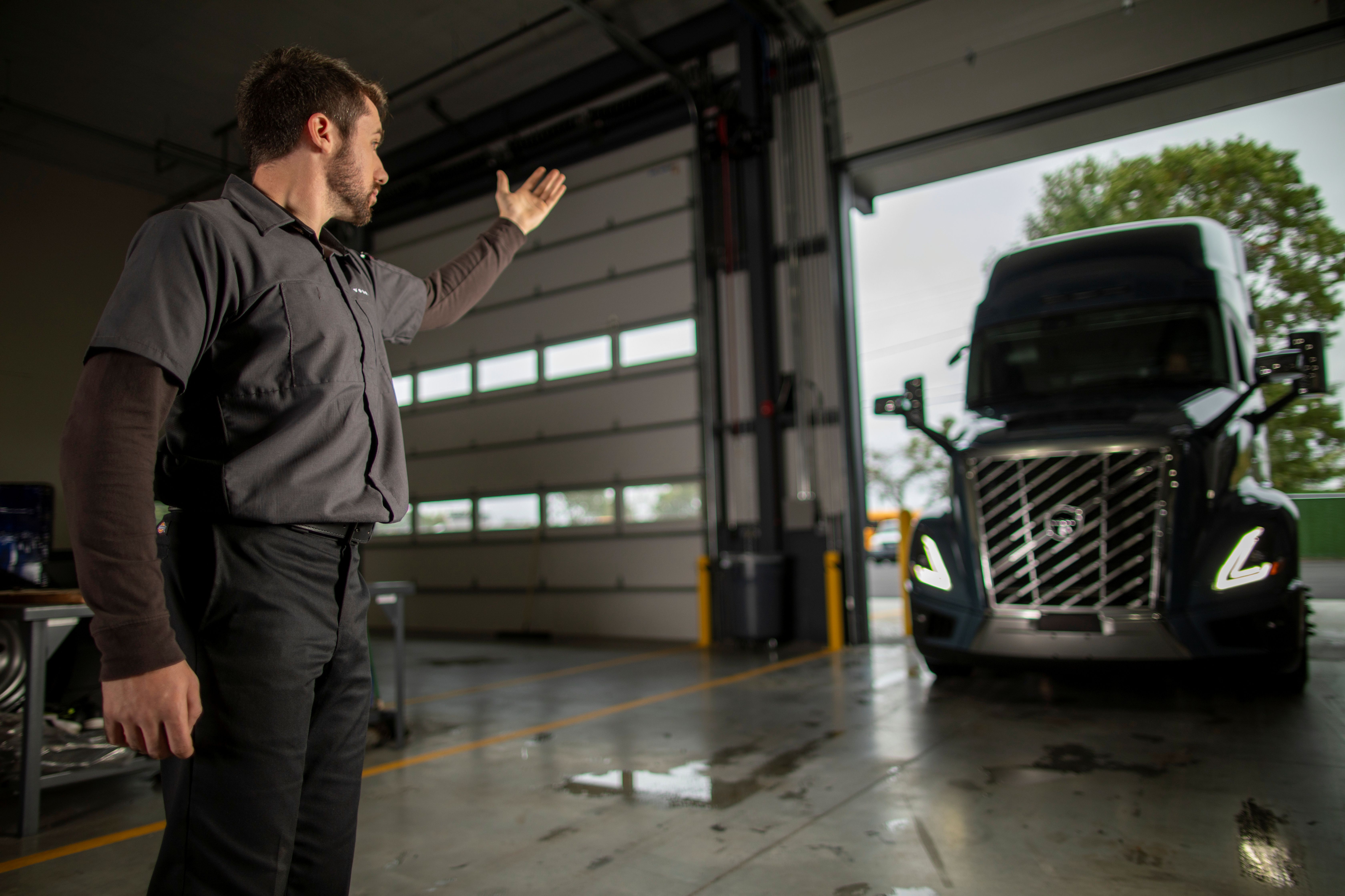Mechanic gesturing in truck garage with commercial vehicle in background