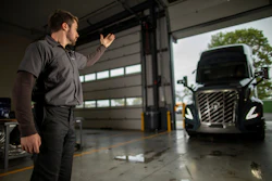 Mechanic gesturing in truck garage with commercial vehicle in background