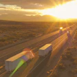 Aerial view of highway with semi-trucks traveling during golden sunset over desert landscape