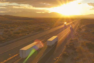 Aerial view of highway with semi-trucks traveling during golden sunset over desert landscape