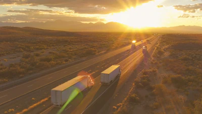 Aerial view of highway with semi-trucks traveling during golden sunset over desert landscape