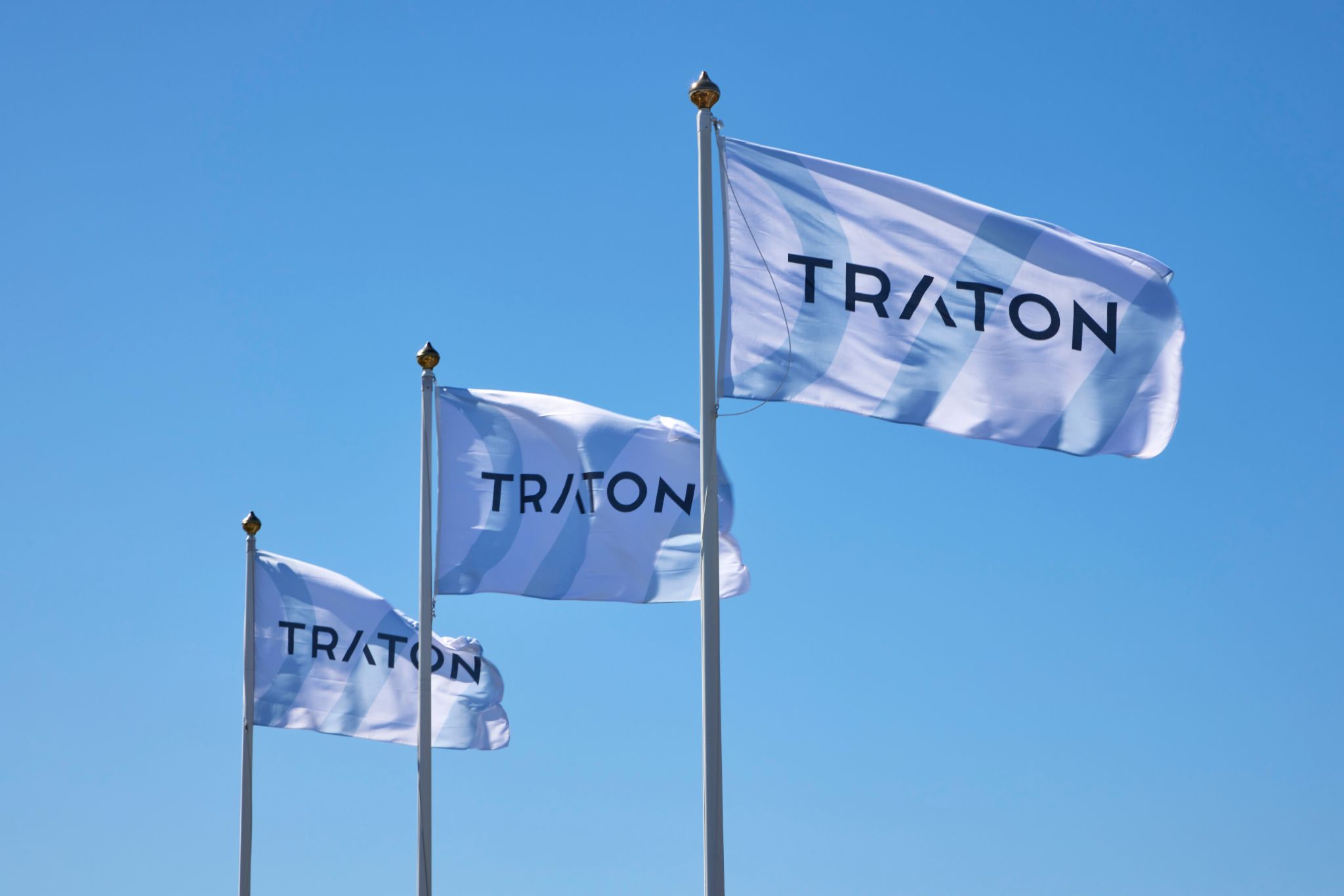Three blue and white TRATON corporate flags flying against a clear sky