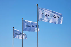 Three blue and white TRATON corporate flags flying against a clear sky