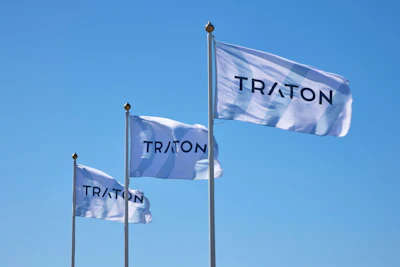 Three blue and white TRATON corporate flags flying against a clear sky