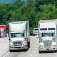 White commercial trucks driving on a multi-lane highway with dense green forest in the background