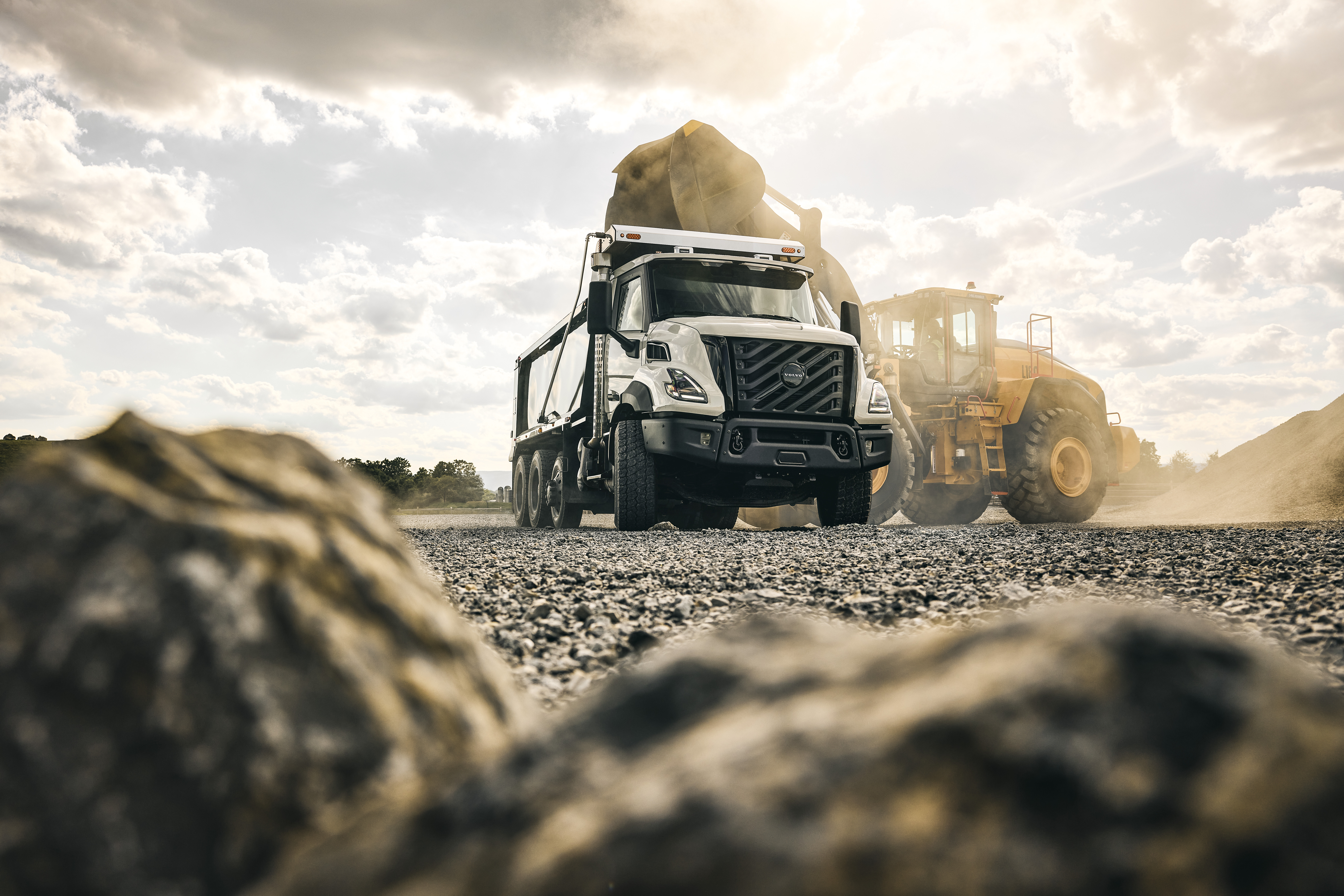 Concrete mixer truck and wheel loader working on gravel construction site under cloudy sky