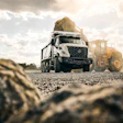 Concrete mixer truck and wheel loader working on gravel construction site under cloudy sky
