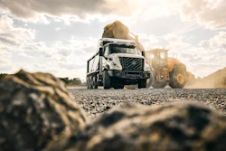 Concrete mixer truck and wheel loader working on gravel construction site under cloudy sky
