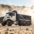 White and black dump truck hauling gravel on dusty construction site with hills in background