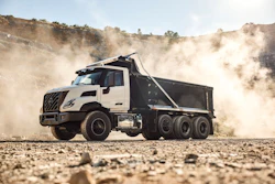 White and black dump truck hauling gravel on dusty construction site with hills in background