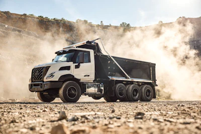 White and black dump truck hauling gravel on dusty construction site with hills in background