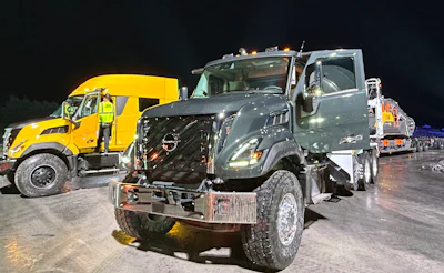 Commercial trucks lined up at night, including yellow Volvo and gray Nissan vehicles in fleet formation