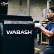 Worker in blue shirt performing maintenance on black Wabash industrial equipment in warehouse setting