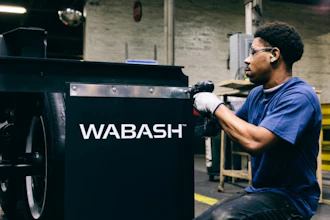 Worker in blue shirt performing maintenance on black Wabash industrial equipment in warehouse setting