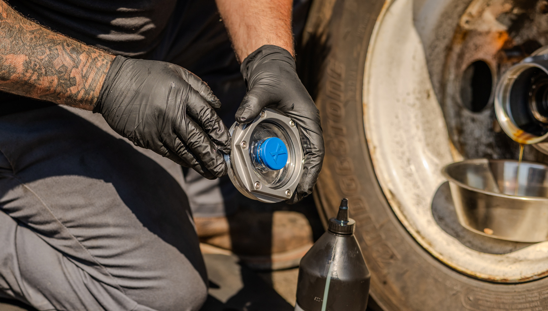 Mechanic wearing black gloves installing or removing a blue wheel hub cap on a vehicle during maintenance