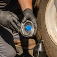 Mechanic wearing black gloves installing or removing a blue wheel hub cap on a vehicle during maintenance