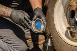 Mechanic wearing black gloves installing or removing a blue wheel hub cap on a vehicle during maintenance