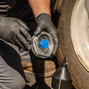 Mechanic wearing black gloves installing or removing a blue wheel hub cap on a vehicle during maintenance